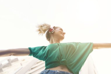 Şehirde dans eden ve kulaklık takan genç ve neşeli bir kadın.