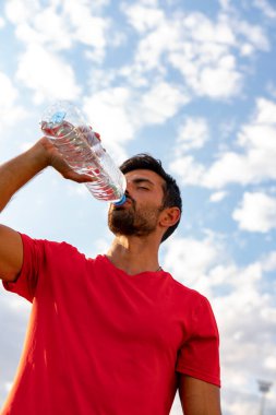Adam spordan sonra açık havada su içiyor.