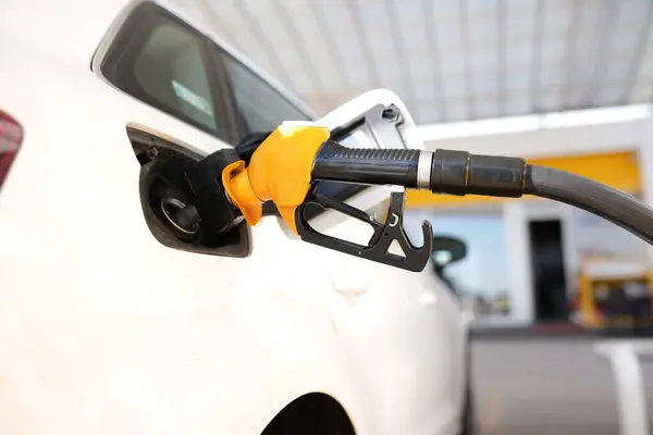 Benzin istasyonunda bir araba dolduruluyor. Benzin pompası siyah ve gümüş.