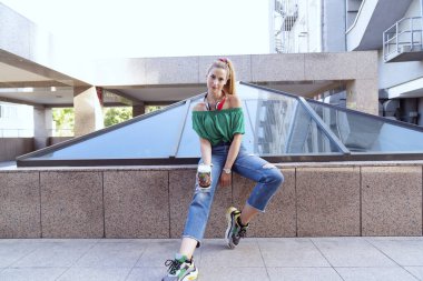 Genç bir kadın şehirde kağıt bardakla kahve içiyor.