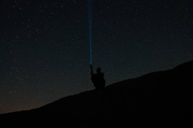 Gece gökyüzündeki parlak yıldızlar ve takımyıldızları yıldızlı gökyüzünün arka planında bir adamın silueti bir feneri gökyüzüne tutar ve yıldızları aydınlatmaya çalışır.