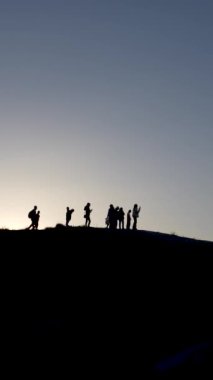 Bir grup insan alacakaranlıkta bir yamaçta dikiliyorlar. Dağın tepesindeki insanların siluetleri.