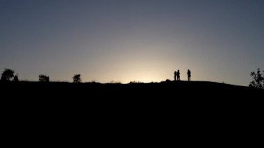 Bir grup insan alacakaranlıkta bir yamaçta dikiliyorlar. Dağın tepesindeki insanların siluetleri.