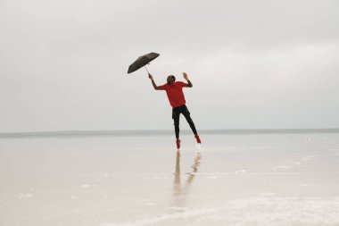 Şemsiyeyle havaya atlayan bir adamın sudaki yansıması.