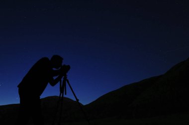 Gece gökyüzünün fotoğraflarını çeken bir fotoğrafçı. İnsan silueti, yıldızlı gökyüzünün arka planına karşı. Yıldızlar