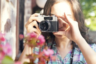 Genç bir kadın yaşlı bir kamerayı tutuyor ve ekrandan bakıyor.      