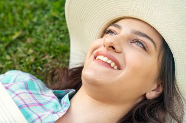 Güzel genç bir kadın çimlere uzanıp kitap okuyor..         