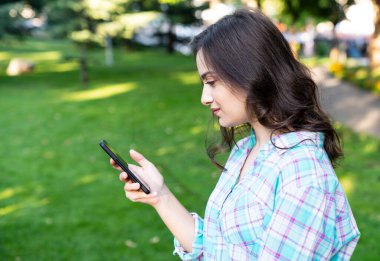 Kadın parkta dinleniyor ve akıllı telefonunu kullanıyor..