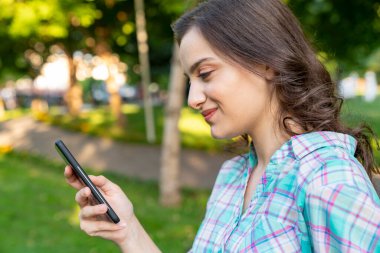 Kadın parkta dinleniyor ve akıllı telefonunu kullanıyor..