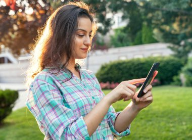 Kadın parkta dinleniyor ve akıllı telefonunu kullanıyor..