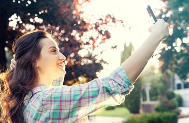 Genç ve güzel bir kadın gün batımında parkta selfie çekiyor.
