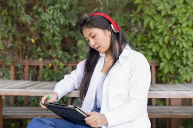 Genç ve güzel Asyalı bir kadın internette / laptopta çalışıyor açık hava parkında alışveriş yapıyor.,