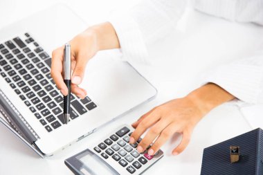 Emlakçı ofiste dizüstü bilgisayarla çalışıyor. El bilgisayarı ve hesap makinesi kullanıyor.