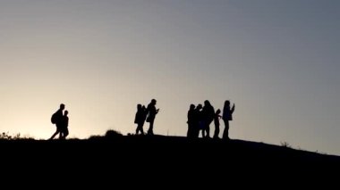 Alacakaranlıkta tepenin yamacında duran bir grup insan. Dağın tepesindeki insanların siluetleri.