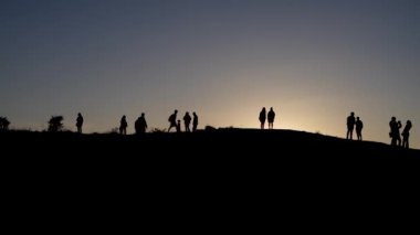 Alacakaranlıkta tepenin yamacında duran bir grup insan. Dağın tepesindeki insanların siluetleri.
