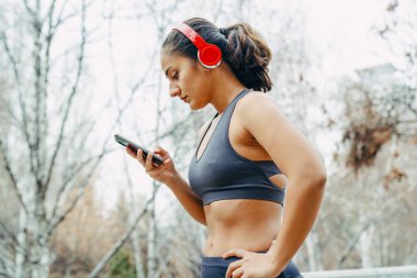 Spor yaptıktan sonra spor salonuna gelen genç bir kadın. Kulaklıklar ve akıllı telefonlar ile spor konsepti.