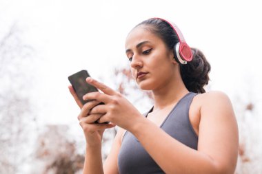 Spor yaptıktan sonra spor salonuna gelen genç bir kadın. Kulaklıklar ve akıllı telefonlar ile spor konsepti.