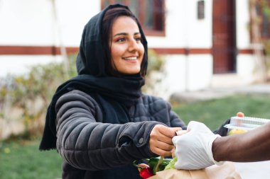 Genç Ortadoğulu kadın gönüllü yemek dağıtıyor. Market teslimat servisi.