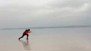 Arka planda güneş batarken bir adam plajda koşuyor.