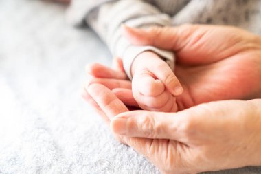 Bir bebeğin eli bir ebeveyn tarafından tutuluyor. Aile sevgisi ve koruma kavramı.
