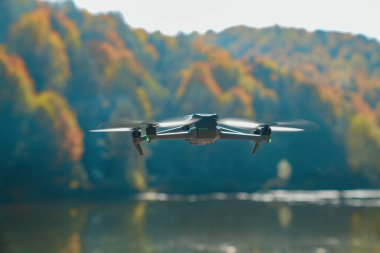 Arka planda ağaçlar olan bir dron gölün üzerinde uçuyor.