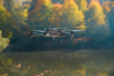 Arka planda ağaçlar olan bir dron gölün üzerinde uçuyor.