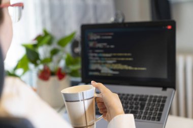 Kadın kahve içerken dizüstü bilgisayarda çalışıyor.