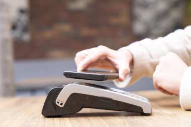 Kafede alışveriş, satış veya çıkış için kasiyer ile birlikte akıllı telefon, makine veya müşterinin elleri.