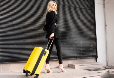 Bir iş kadını elinde bavulla sokakta yürüyor.