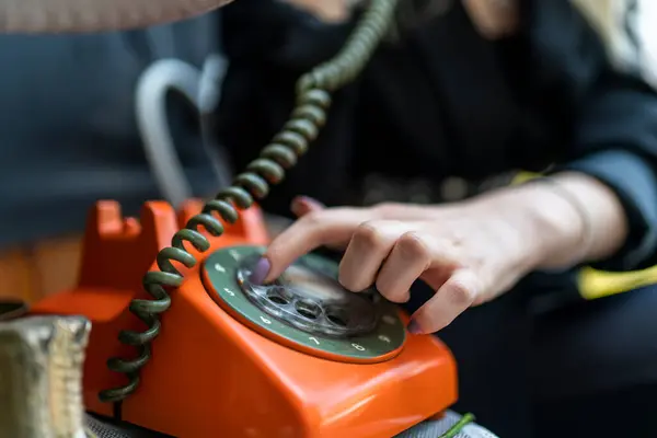 Eski turuncu döner telefonu ahşap retro masa üzerinde telefonla tutarken yakın plan. Vintage döner telefon konsepti.