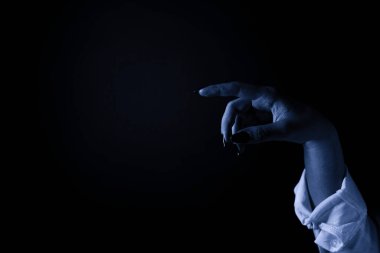 Karanlıkta bir şeyi işaret eden bir el. Eli siyah ojeyle kaplanmış ve tırnakları siyaha boyanmış.