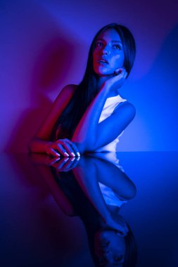 Renkli parlak neon ışıklarıyla stüdyoda poz veren yüksek model kadın. Parlak makyajlı güzel bir kadının portresi. Sanat tasarımı canlı biçimi