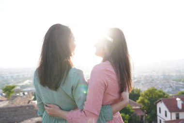 Genç bayan arkadaşlar güneşli şehir manzarasını izliyor