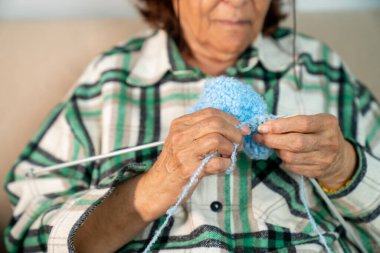 Yaşlı kadın örgü örüyor, pencerenin yanındaki koltuğunda oturuyor.