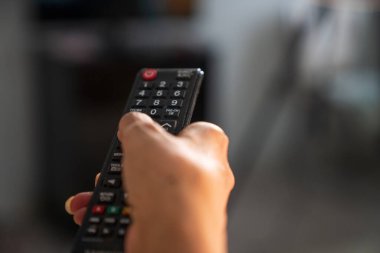 Evde televizyon seyrederken elinde uzaktan kumanda tutan olgun bir kadın.