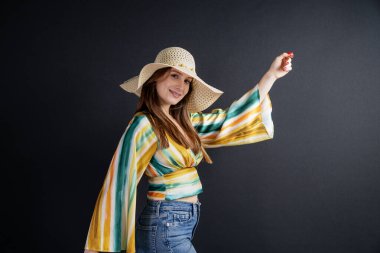 Siyah arka planda hasır şapkalı mutlu bir genç kadın.