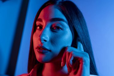 Renkli parlak neon ışıklarıyla stüdyoda poz veren yüksek model kadın. Parlak makyajlı güzel bir kadının portresi. Sanat tasarımı canlı biçimi