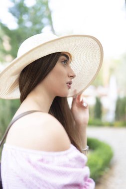 Hasır şapkalı genç bir kadın sokakta yürüyor.