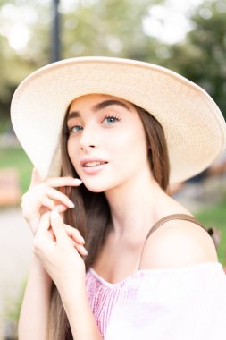 Hasır şapkalı genç bir kadın sokakta yürüyor.