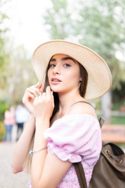 Hasır şapkalı genç bir kadın sokakta yürüyor.