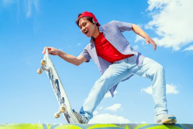 Genç adam arka planda mavi ve bulutlu bir kaykayla mutlu poz veriyor. gençlik sporları ve eğlence konsepti