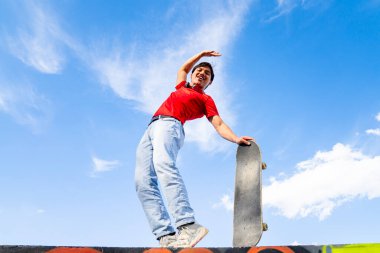 Genç adam arka planda mavi ve bulutlu bir kaykayla mutlu poz veriyor. gençlik sporları ve eğlence konsepti