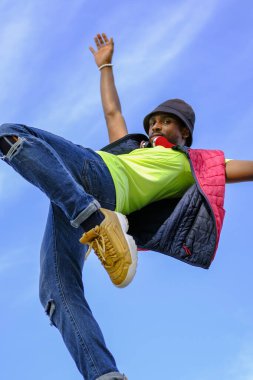 Kolları açık bir adam havaya zıplıyor. Gökyüzü mavi ve arka planda bulutlar var. Manzara neşeli ve enerjik.