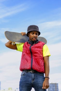 Genç adam arka planda mavi ve bulutlu bir kaykayla mutlu poz veriyor. gençlik sporları ve eğlence konsepti