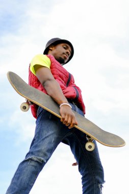 Genç adam arka planda mavi ve bulutlu bir kaykayla mutlu poz veriyor. gençlik sporları ve eğlence konsepti