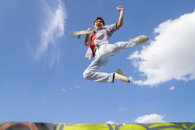 Kolları açık bir adam havaya zıplıyor. Gökyüzü mavi ve arka planda bulutlar var. Manzara neşeli ve enerjik.