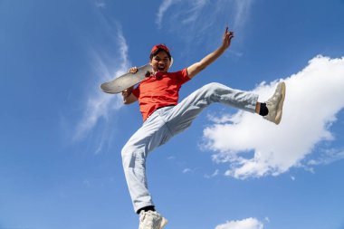 Kolları açık bir adam havaya zıplıyor. Gökyüzü mavi ve arka planda bulutlar var. Manzara neşeli ve enerjik.