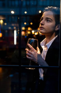 Pencerenin önünde şarap kadehi tutan genç bir kadın.