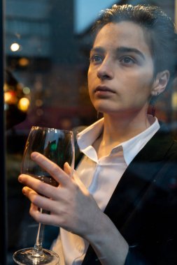 Pencerenin önünde şarap kadehi tutan genç bir kadın.