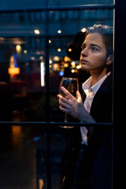 Pencerenin önünde şarap kadehi tutan genç bir kadın.
